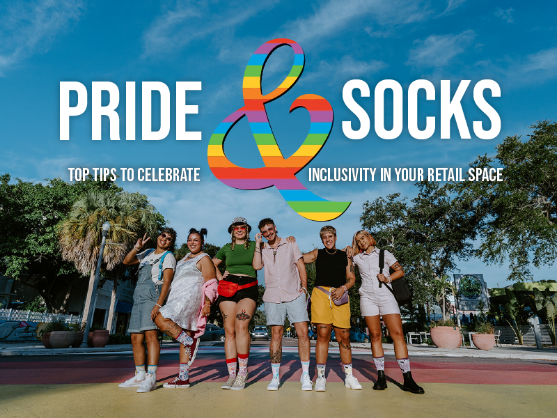 Photograph of six people standing in a line facing the camera on a rainbow colored sidewalk. They all wear Socksmith Pride Roses socks. The text says "Pride & Socks: Top tips to celebrate inclusivity in your retail space"