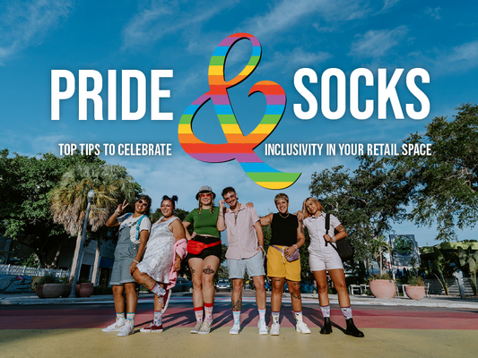 Photograph of six people standing in a line facing the camera on a rainbow colored sidewalk. They all wear Socksmith Pride Roses socks. The text says "Pride & Socks: Top tips to celebrate inclusivity in your retail space"
