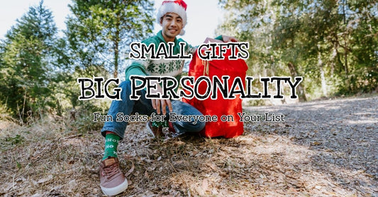Fun novelty socks as stocking stuffers [image of man carrying santa sack wearing Ho Ho Ho socks in green]