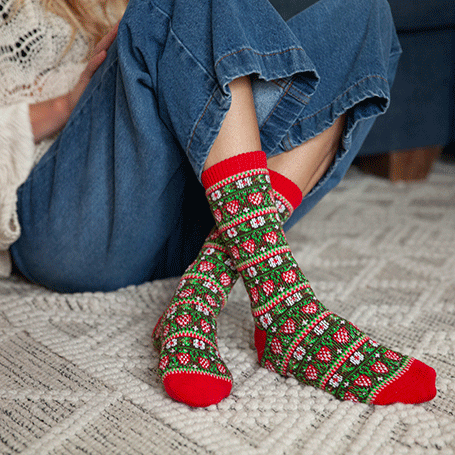 Person wearing festive patterned socks with red toes on a textured floor.