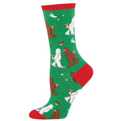 A pair of green and red crew socks with a pattern of yetis and bigfoots wearing Christmas hats.