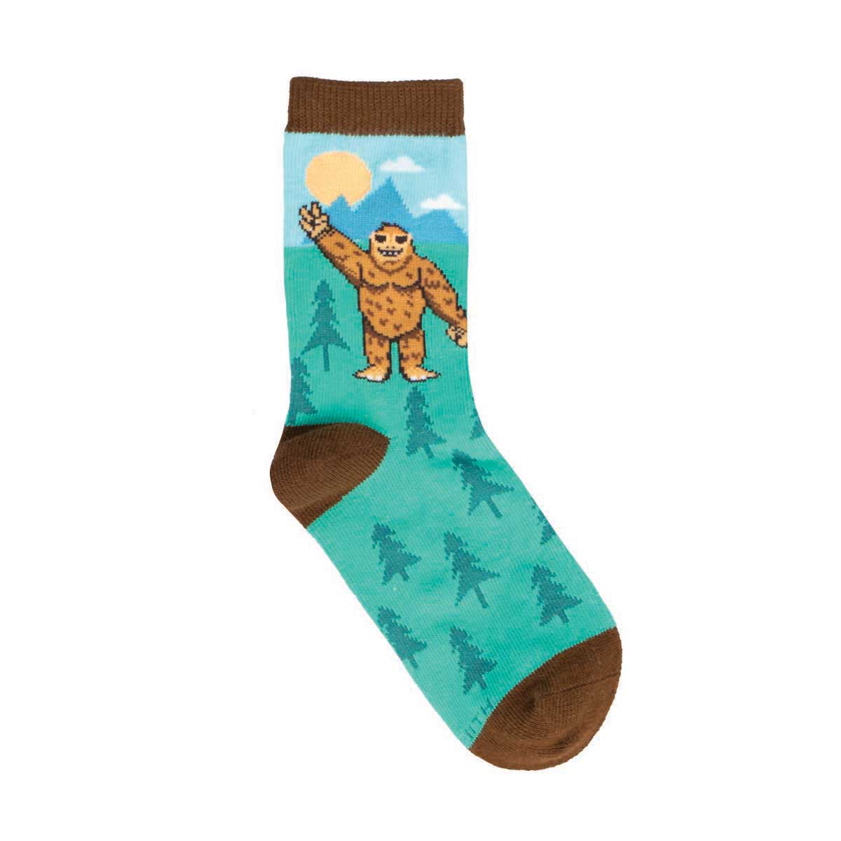 A colorful kids sock with a Bigfoot design, featuring a green background with trees and a brown cuff.