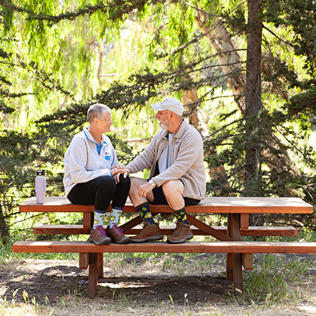 Two people sitting on a wooden bench in a forest setting