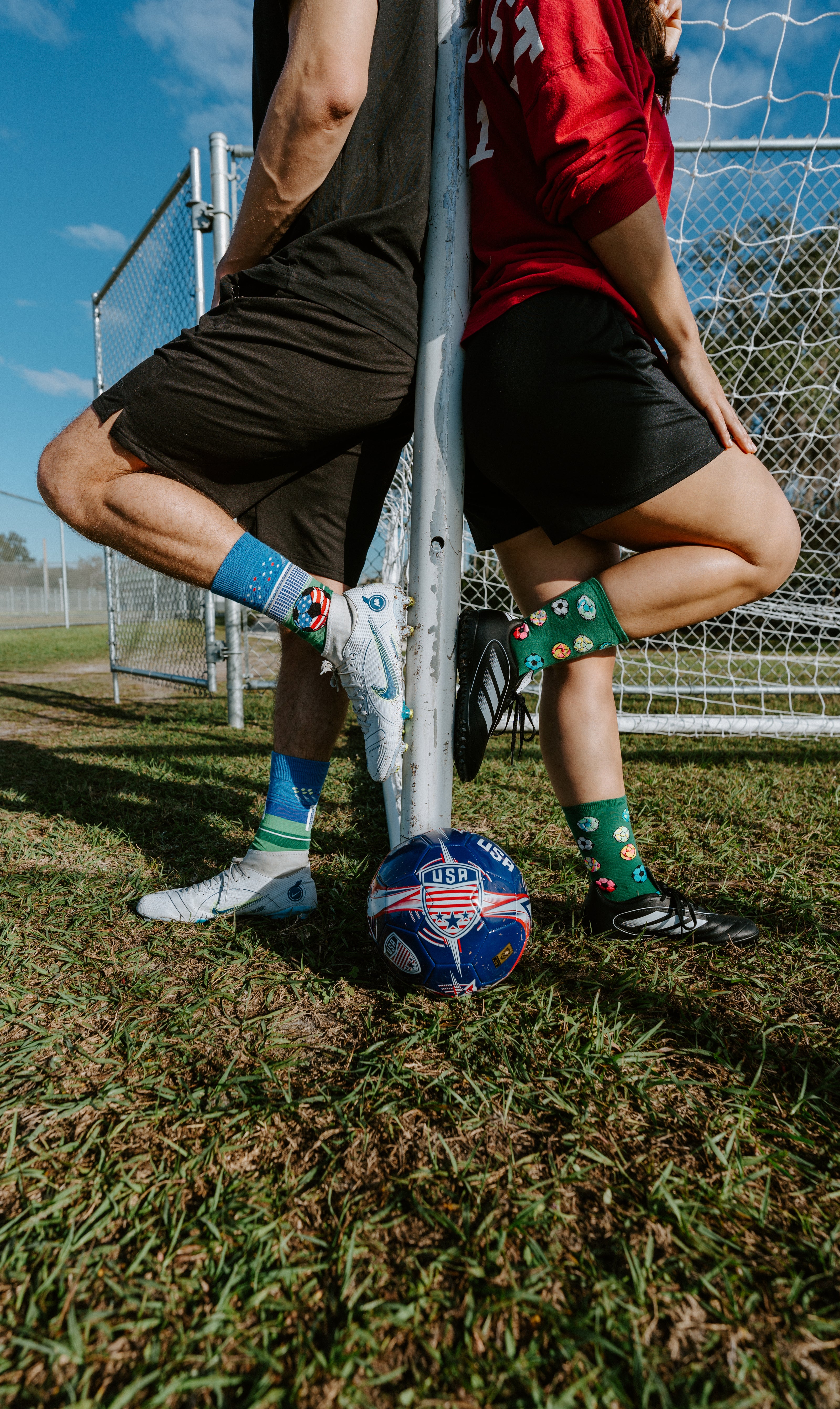 "two people leaning against soccer goal post wearing soccer socks"
