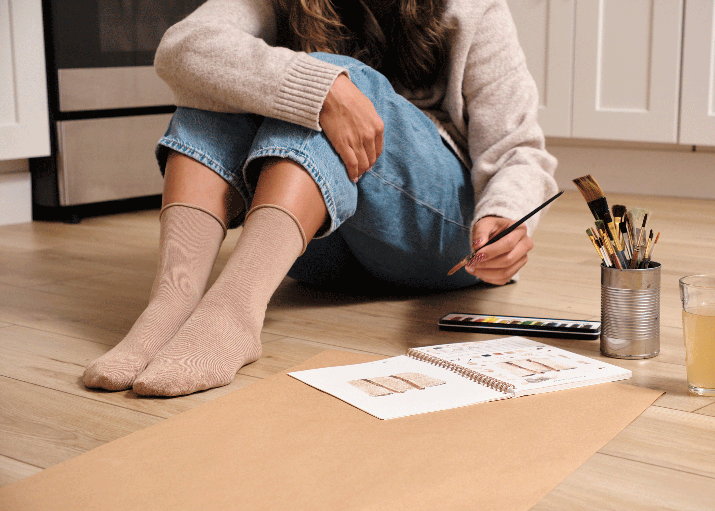 Person sitting on the floor with art supplies in a kitchen wearing khaki bamboo socks with roll top