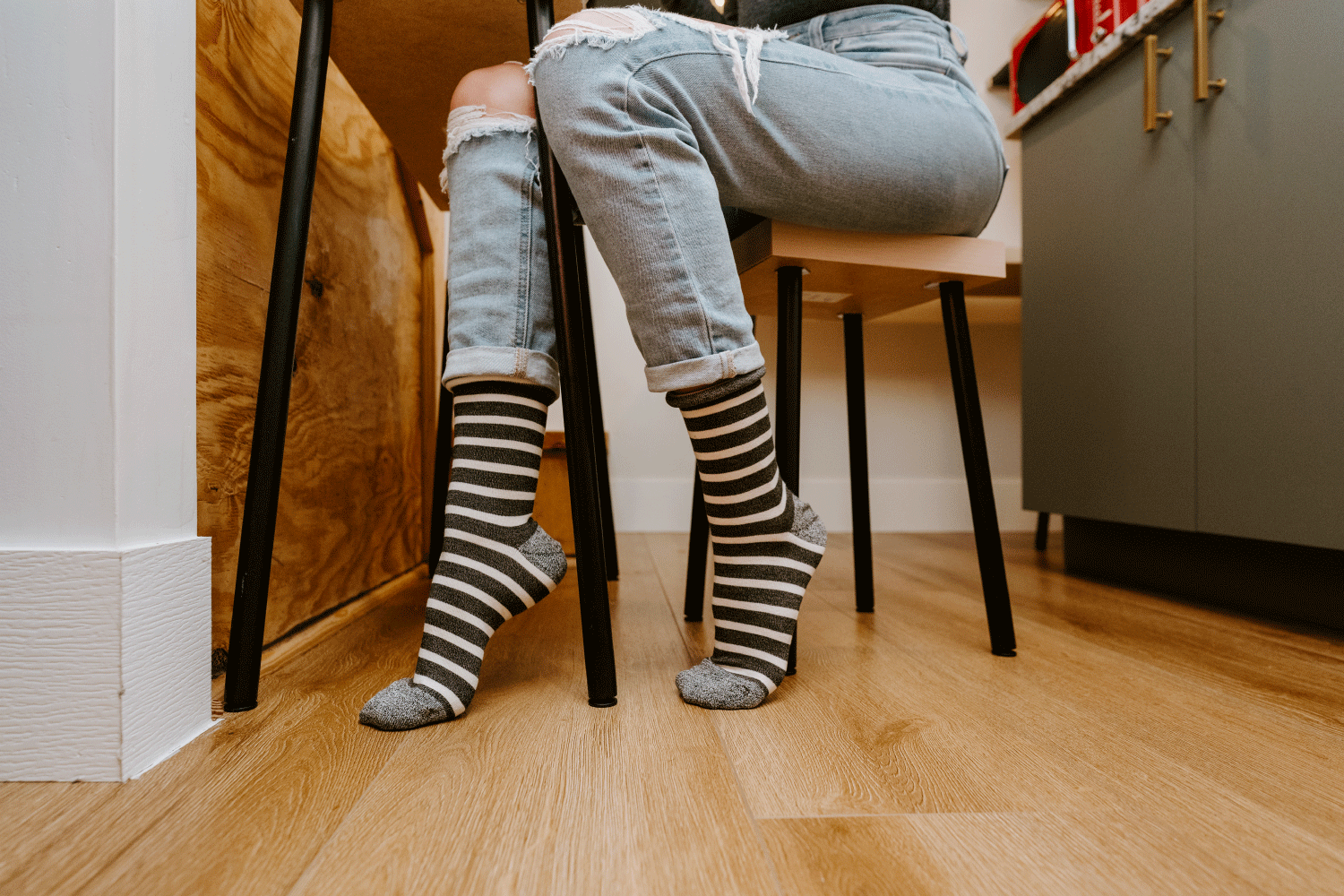 A person wearing striped gray and white bamboo socks sitting at a desk on a low wooden stool.