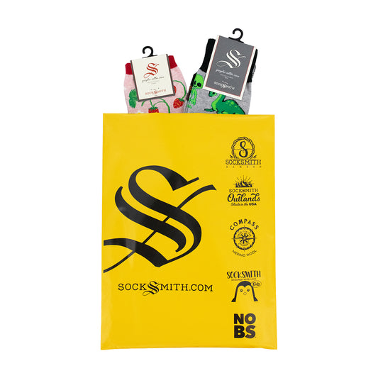 A yellow Socksmith gift bag with black printed logos and text, holding two packaged pairs of cotton novelty socks, one men's and one women's.